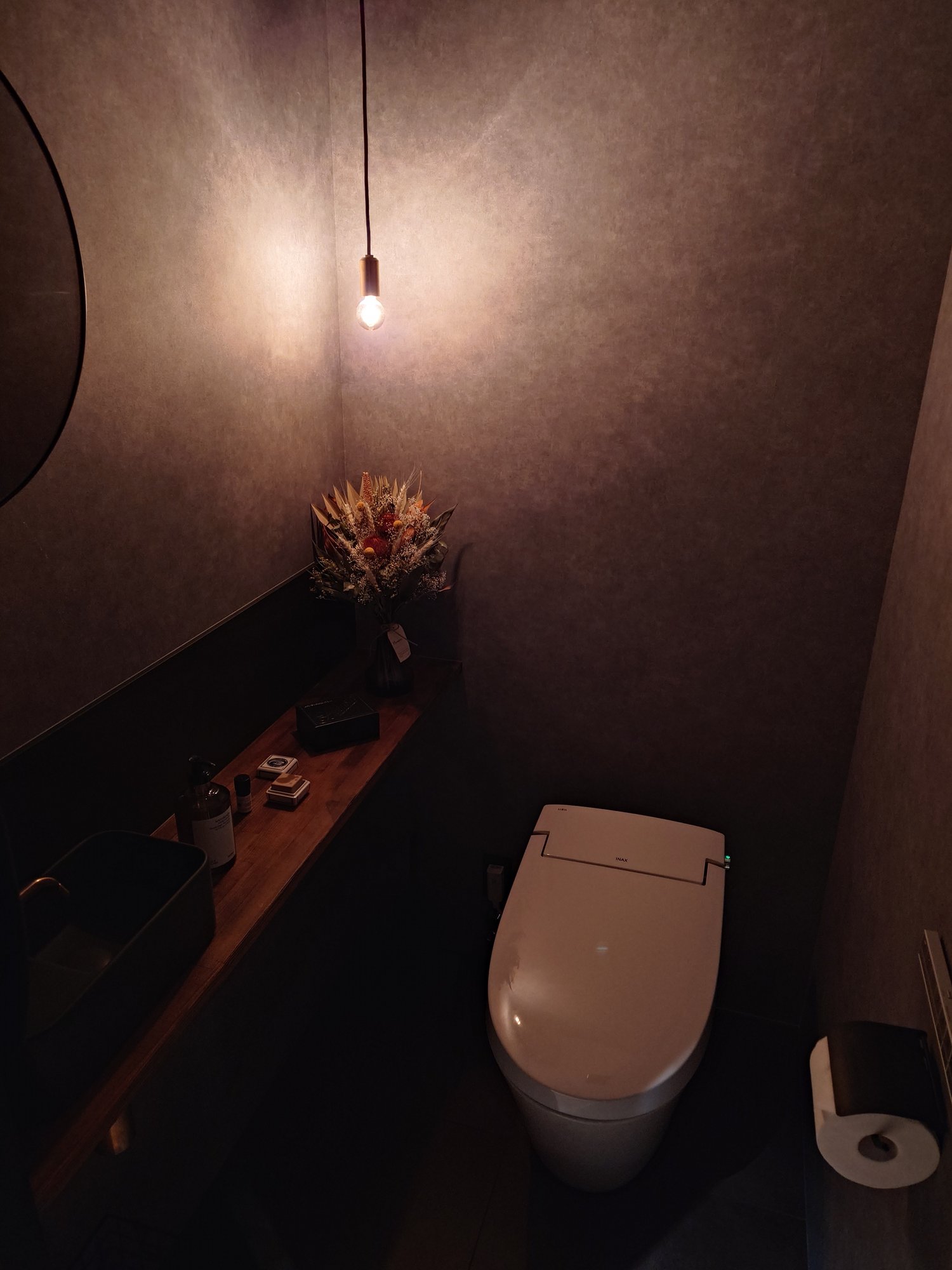 別アングルから見たトイレ個室。木の造作カウンターとペンダントライトが並ぶ。