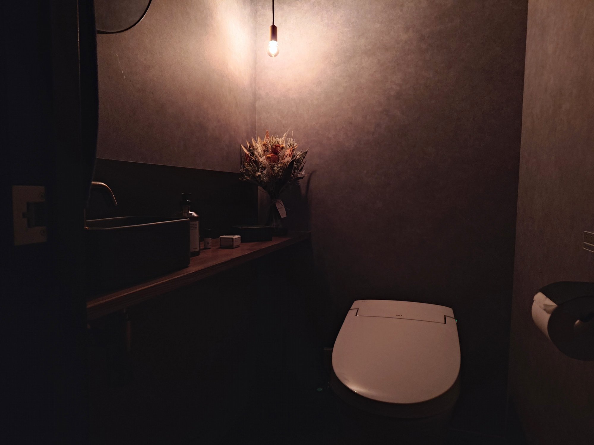 照度を落としたトイレ個室。真鍮のペンダントライトとドライフラワーで柔らかい陰影を作っている。